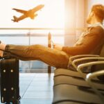 Επιβάτης περιμένει την πτήση του στην αίθουσα αναμονής αεροδρομίου με α πόδια στη βαλίτσα του