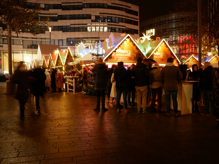 A mulled wine stand at a German Christmas market with warm lights and visitors ordering drinks.