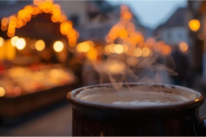Steaming mug of Glühwein at Nuremberg’s Christkindlesmarkt with festive lights behind